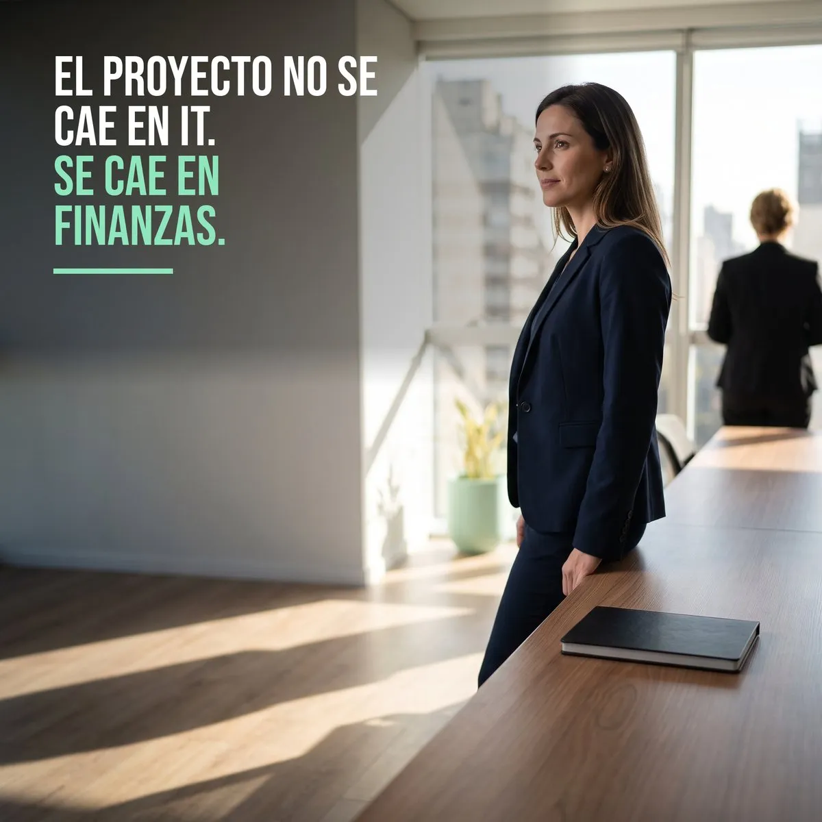 Ejecutiva de pie junto al ventanal de una sala de directorio, con una notebook cerrada sobre la mesa